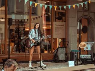 Eine Frau mit Gitarre hat ein Konzert in der Laube vor dem Visitor Centre in der Stadt Schaffhausen.