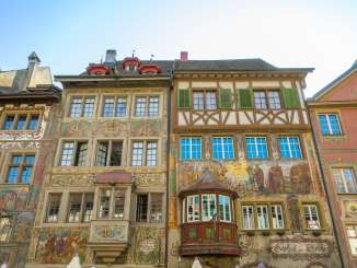 Vier Häuser mit alten bemalten Fassaden. Ebenfalls sind zwei Erker zu sehen, welche hervorstehen.