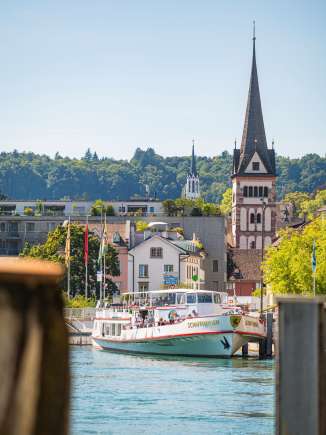 Das Kursschiff der URh ist in Schaffhausen angelegt. Im Hintergrund sieht man einen Kirchenturm.
