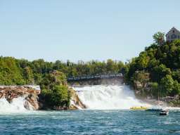 Ein Zug fährt über die Eisenbahnbrücke hinter dem Rheinfall in Richtung Schloss Laufen.